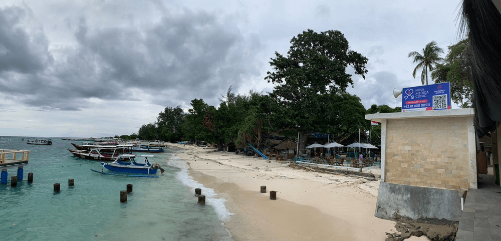 Coastal view of gili air harbour with traditional boats, clear turquoise water, and beachfront area near the main arrival point on Gili Air island.