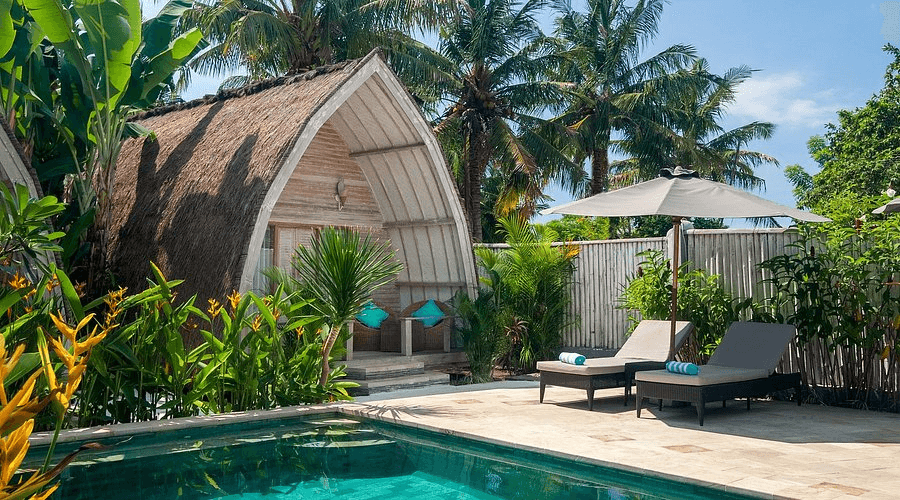 Tropical Gili Air bungalows surrounded by palm trees and lush garden near a private swimming pool, showcasing a relaxing island accommodation atmosphere in Gili Air, Lombok.