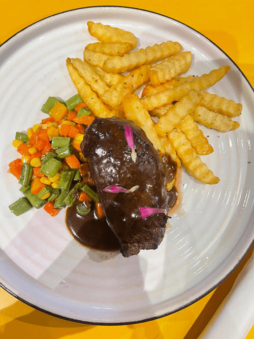 Grilled steak with crinkle-cut fries and mixed vegetables served on a plate, showcasing delicious Gili Air food options for travelers