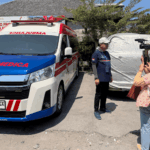 Operational Director PT Nusa Medica Assistama dr. I Gde Yudha Kurniawan during a media interview beside a Nusa Medica ambulance.