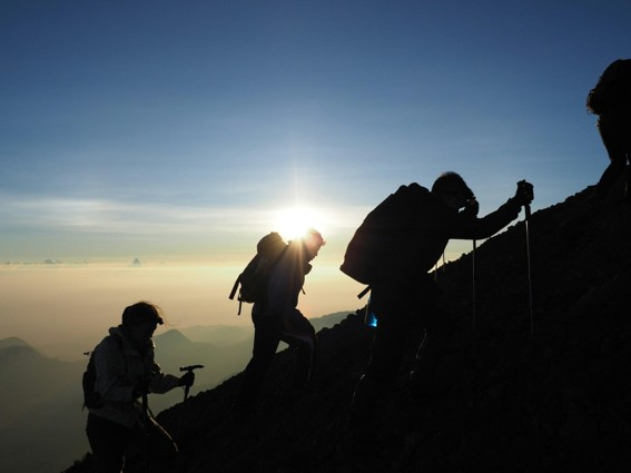 Mount Rinjani hiking trails with hikers climbing a steep mountain route during sunrise.