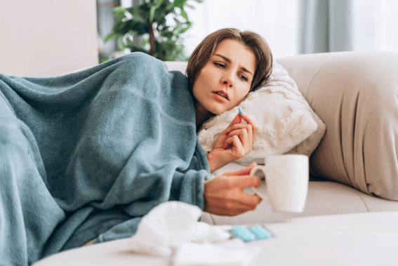 What to Do If You Get Sick in Bali – a sick traveler resting on a sofa while checking her temperature.